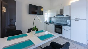 A modern kitchen with white cabinets, a black oven, and a flat-screen TV mounted above the counter. - Great sea view only 500 metres to the beach (Dramalj)