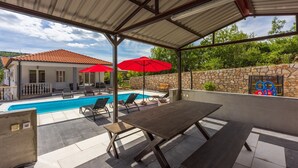 A covered outdoor area with a pool, lounge chairs, and a table.