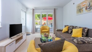 A modern living room with a flat-screen TV, a yellow armchair, a sofa with yellow cushions, and a glass coffee table.