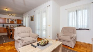 Una sala de estar con dos sillones color beige, una mesa de centro de madera y una cocina al fondo.