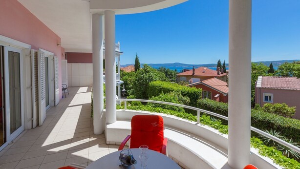 Un balcon avec une table et des chaises, donnant sur une zone côtière avec des maisons et de la végétation.