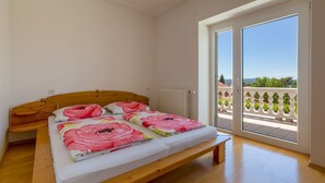 Une chambre avec un lit en bois, du linge de lit blanc et une vue sur un balcon agrémenté de plantes.