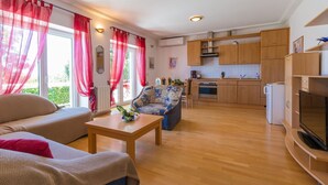 Un salon moderne avec un canapé, une table basse et un téléviseur. La pièce est dotée d’un plancher en bois et on aperçoit une cuisine au fond.