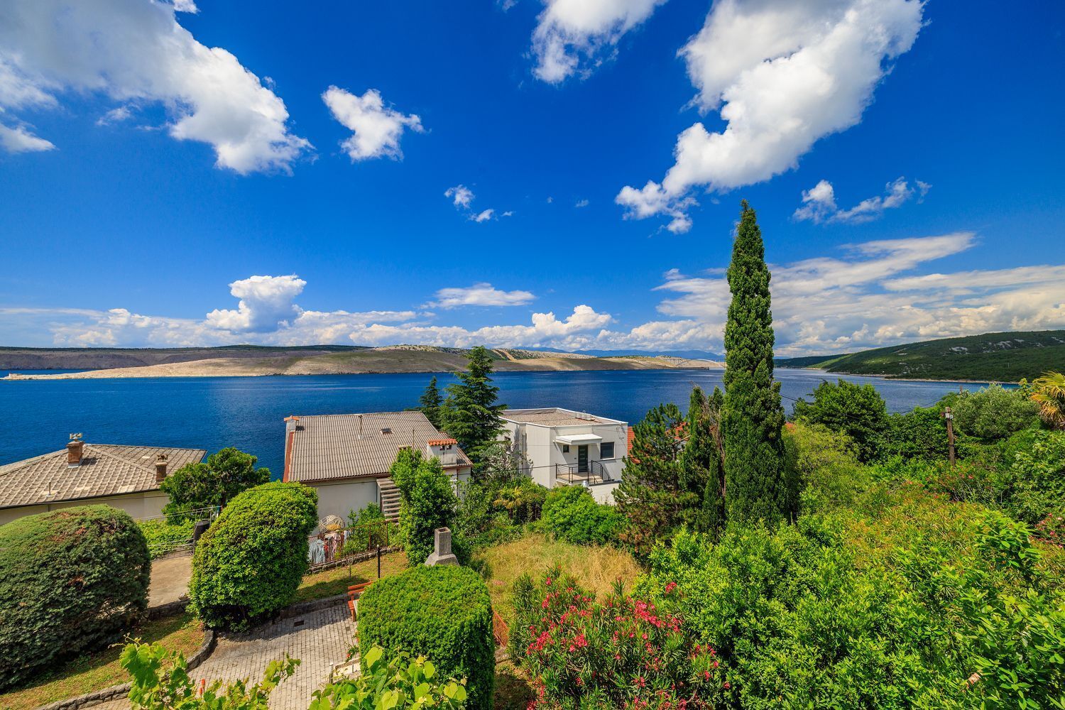 A coastal property with a view of the sea, a garden, and a building with a tiled roof.