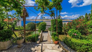 A garden with a stone pathway leading to a gate, surrounded by lush greenery and potted plants. - Only 100 metres to the crystal-clear Adriatic Sea (Jadranovo)