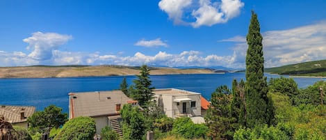 A coastal property with a view of the sea, surrounded by lush greenery and a clear sky.