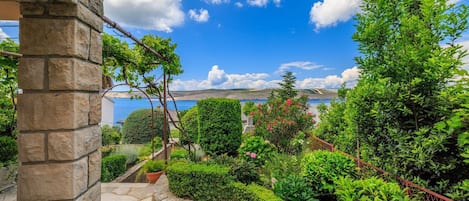 A stone pillar, a garden with various plants, and a view of the sea.