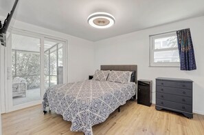 Relax in a stylish bedroom with a large bed and patterned bedspread, a dark dresser, and a window with curtains.