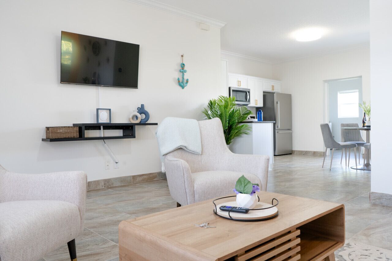 A modern living room with a flat-screen TV, a coffee table, and a dining area with a table and chairs.