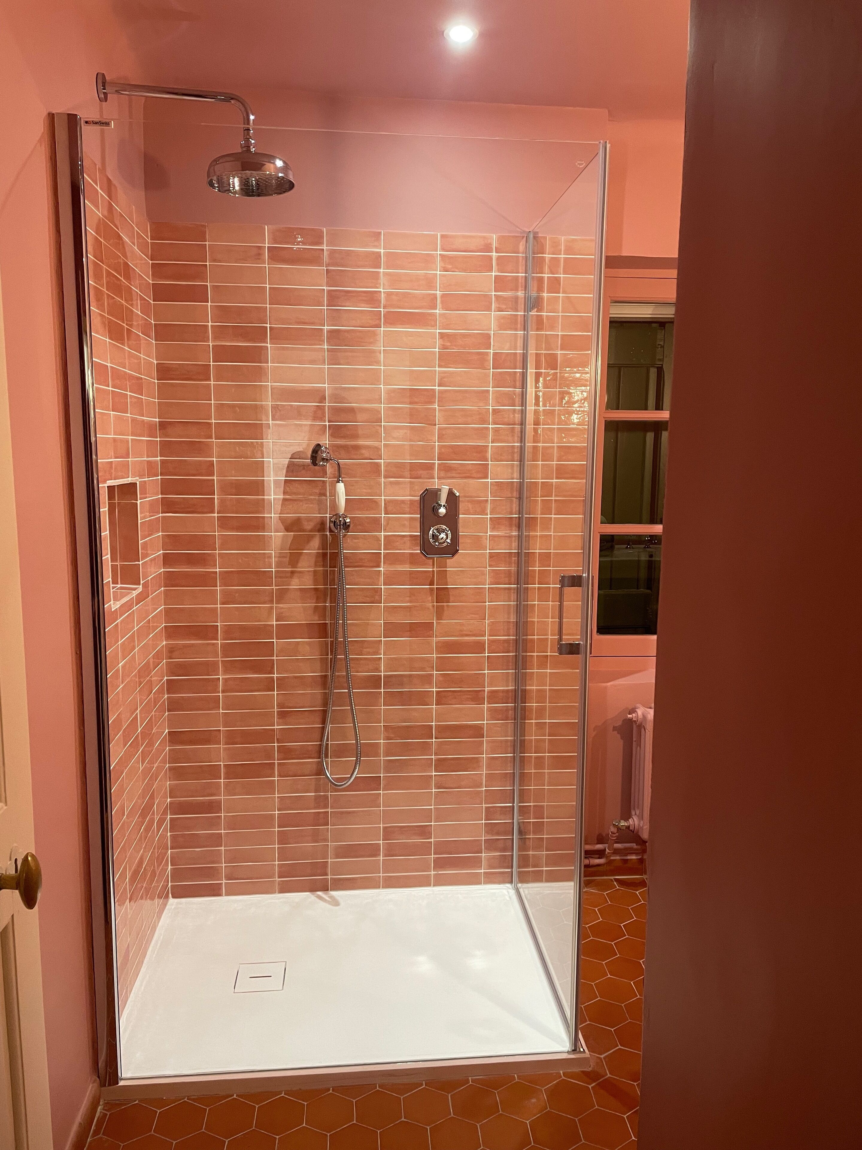 A glass-enclosed shower with a handheld showerhead and a wall-mounted control panel.