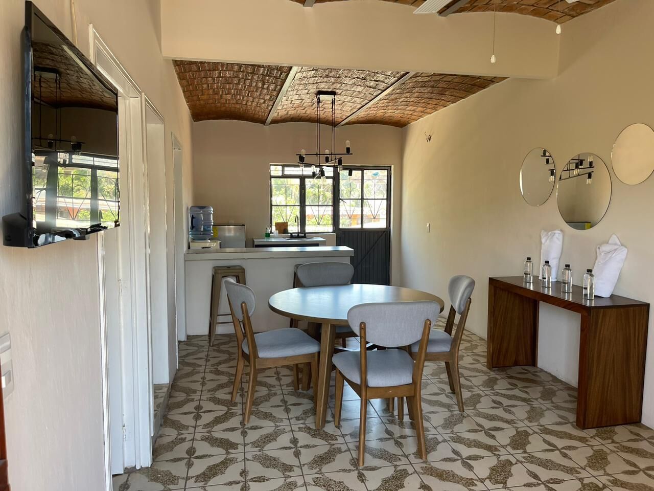 A dining area with a round table and four chairs, a kitchen area with a counter and sink, and a ceiling with exposed beams.