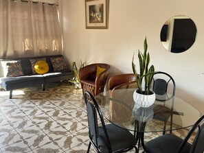 A living room with a sofa, chairs, a glass table, and a potted plant.