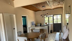 A dining area with a round table and four chairs, a kitchen area with a water dispenser, and a large window with a view of greenery.