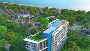 Un edificio moderno de varios pisos con piscina en la azotea, rodeado de vegetación y viviendas residenciales.