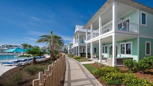 A beachfront hotel with a pool, lounge chairs, and a wooden walkway.