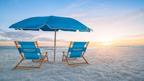 Two blue beach chairs with "Margaritaville" branding on a sandy beach under a blue umbrella.