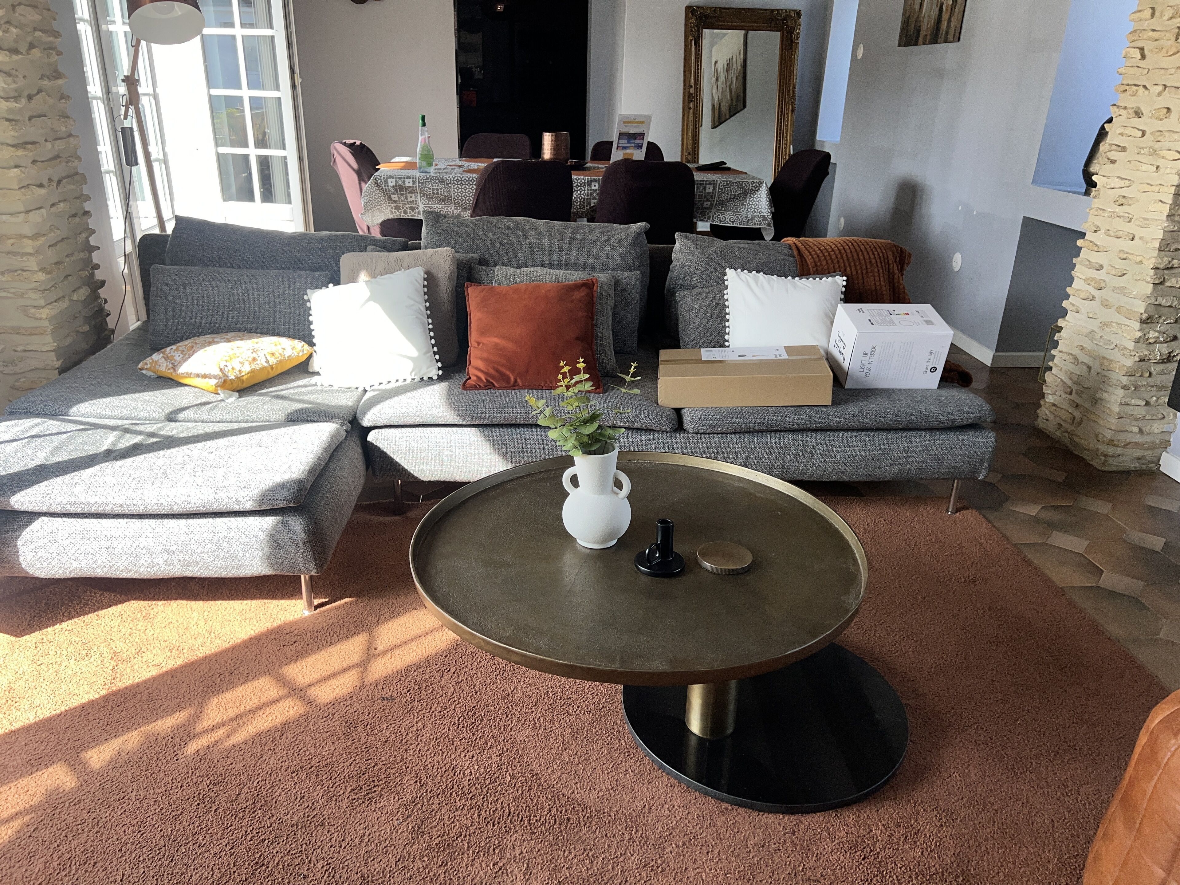 Een moderne woonkamer met een grijze modulaire bank, een salontafel, en een eethoek op de achtergrond.