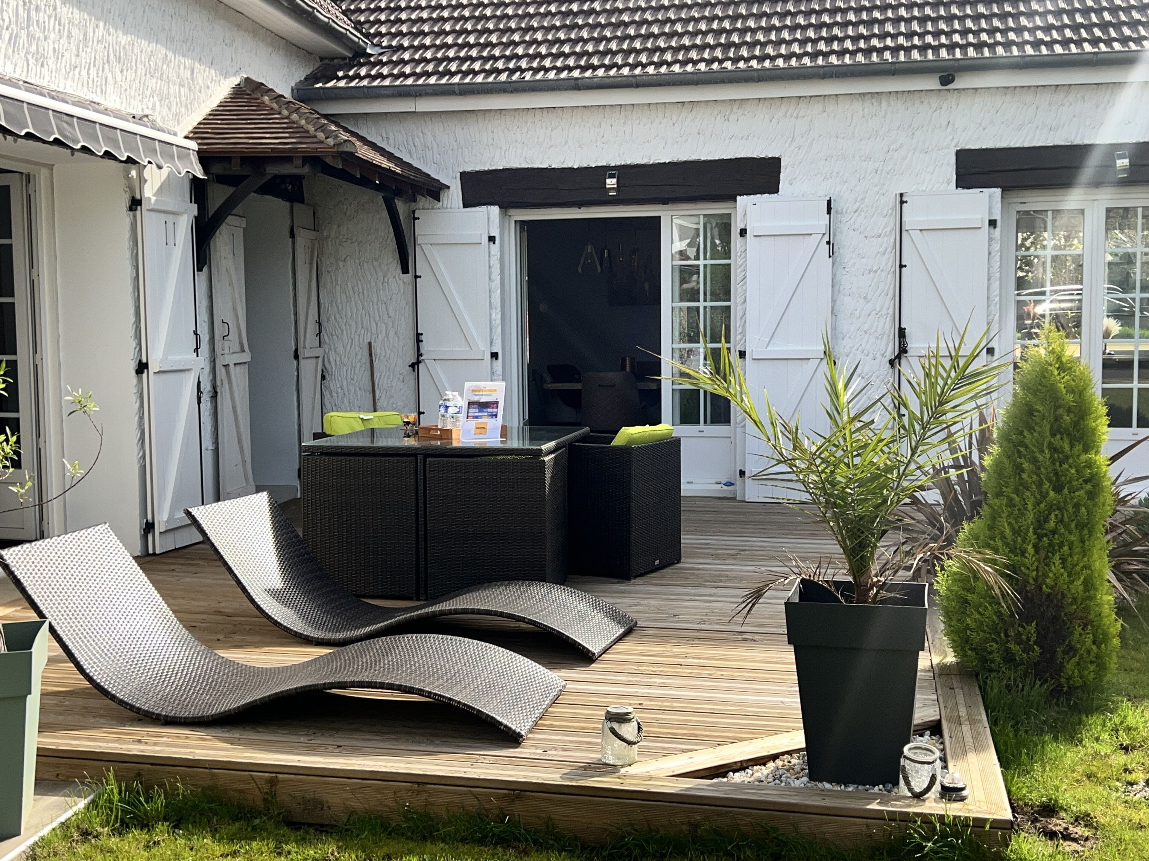A patio area with a wooden deck, two lounge chairs, a small table, and a potted plant.