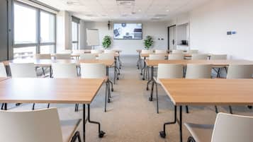 A conference room with multiple tables and chairs, a large screen displaying a presentation, and a whiteboard.