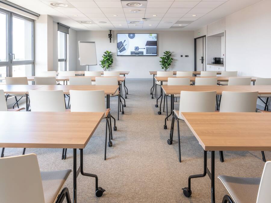 A conference room with multiple tables and chairs, a large screen displaying a presentation, and a whiteboard.