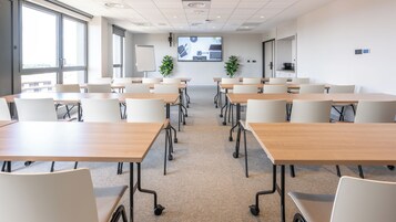 A conference room with multiple tables and chairs, a large screen displaying a presentation, and a whiteboard.