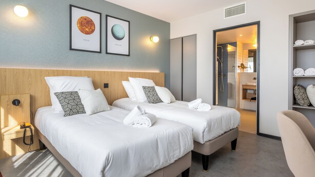 A hotel room with two beds, a wooden headboard, a wardrobe, and a bathroom visible through an open door. - Sevenline Aparthotel Purpan Toulouse (Toulouse)