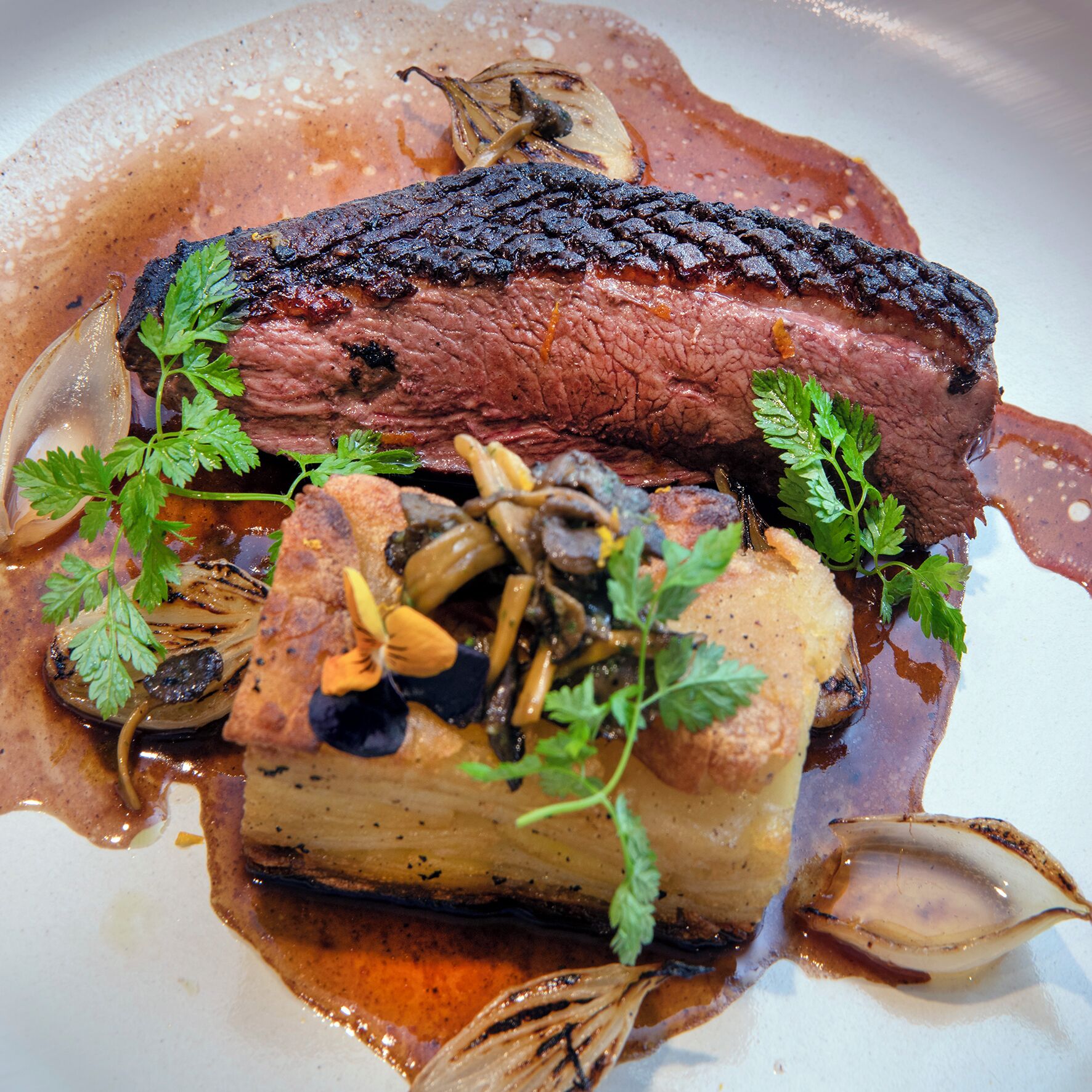 A dish with a piece of meat, vegetables, and herbs.