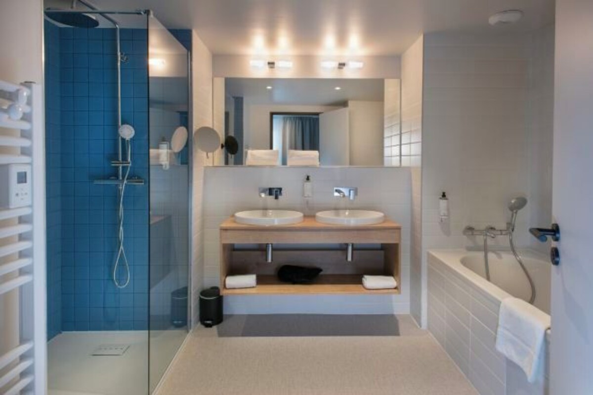A modern bathroom with a glass shower enclosure, two sinks, a bathtub, and a mirror above the sinks.