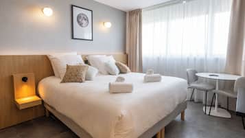 A hotel room with a large bed, bedside tables, a small table with chairs, and a window with curtains.