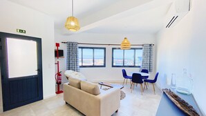 Ein modernes Wohnzimmer mit einer Couch, einem Essbereich mit Stühlen, großen Fenstern und Blick auf die Stadt.