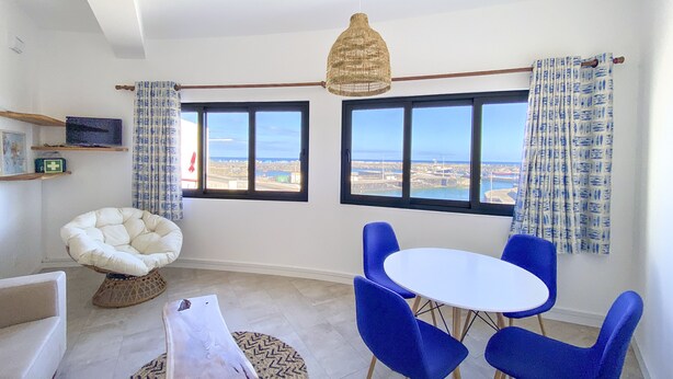 Ein Zimmer mit Meerblick, ein runder Tisch mit blauen Stühlen, ein weißes Sofa und eine Hängelampe.