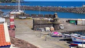 Ein Hafen mit vertäuten Booten, eine steinerne Festung und freie Sicht auf das Meer.