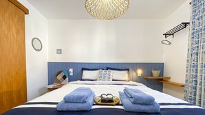 Ein ordentlich bezogenes Bett, blaues Handtuch, ein Nachttisch mit Lampe und eine Pendelleuchte.