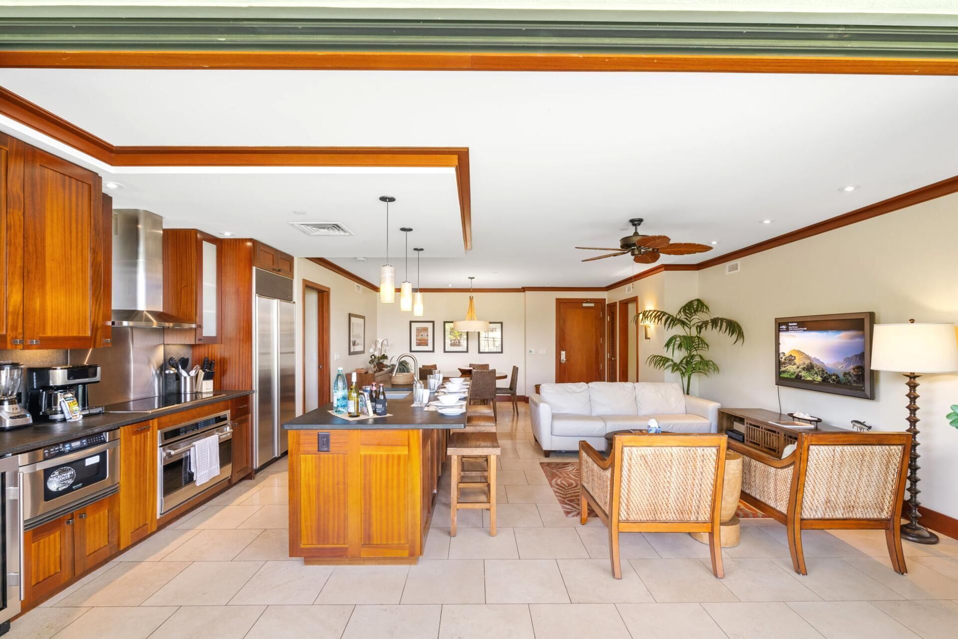 A modern kitchen with a central island, wooden cabinets, stainless steel appliances, and a dining area with a white sofa and wicker chairs.