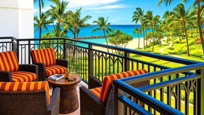 A balcony with wicker furniture, a glass table, and a view of a beach with palm trees and the ocean. - Beach Villas at Ko Olina by KBM (Kapolei)