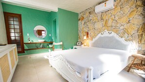 A bedroom with a white bed, a round mirror, a wooden chair, a stone wall, and a door with a frosted glass panel.