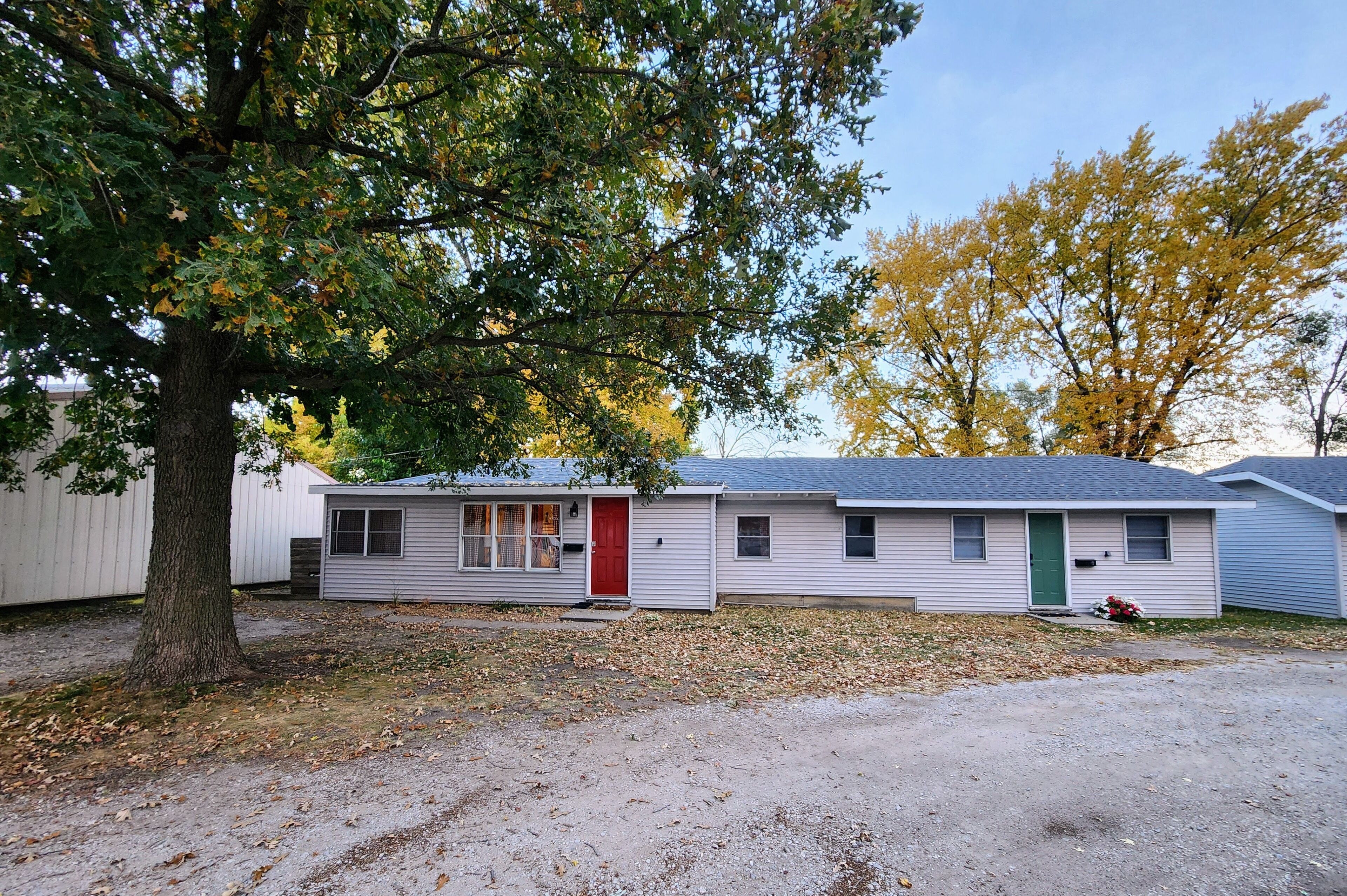 A single-story mobile home with a red door, a small porch, and a tree in front.