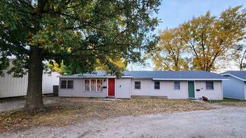 A single-story mobile home with a red door, a small porch, and a tree in front.