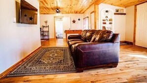 A room with a wooden ceiling, a leather sofa, a patterned rug, and a wall with star decorations. - Knotty Pine Bunkhouse (Nevada)