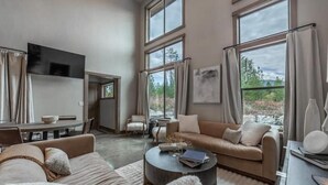 A spacious living room with a large window, a sofa, a coffee table, and a flat-screen TV mounted on the wall.