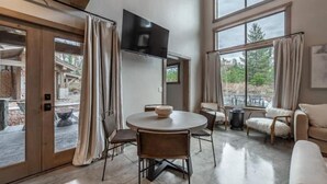 A spacious living area with a round table and chairs, a sofa, and a TV mounted on the wall.