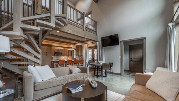 A spacious living area with a high ceiling, a staircase, a kitchen, and a dining area.