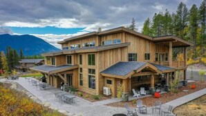A modern wooden cabin with a patio area, outdoor seating, and a view of mountains.