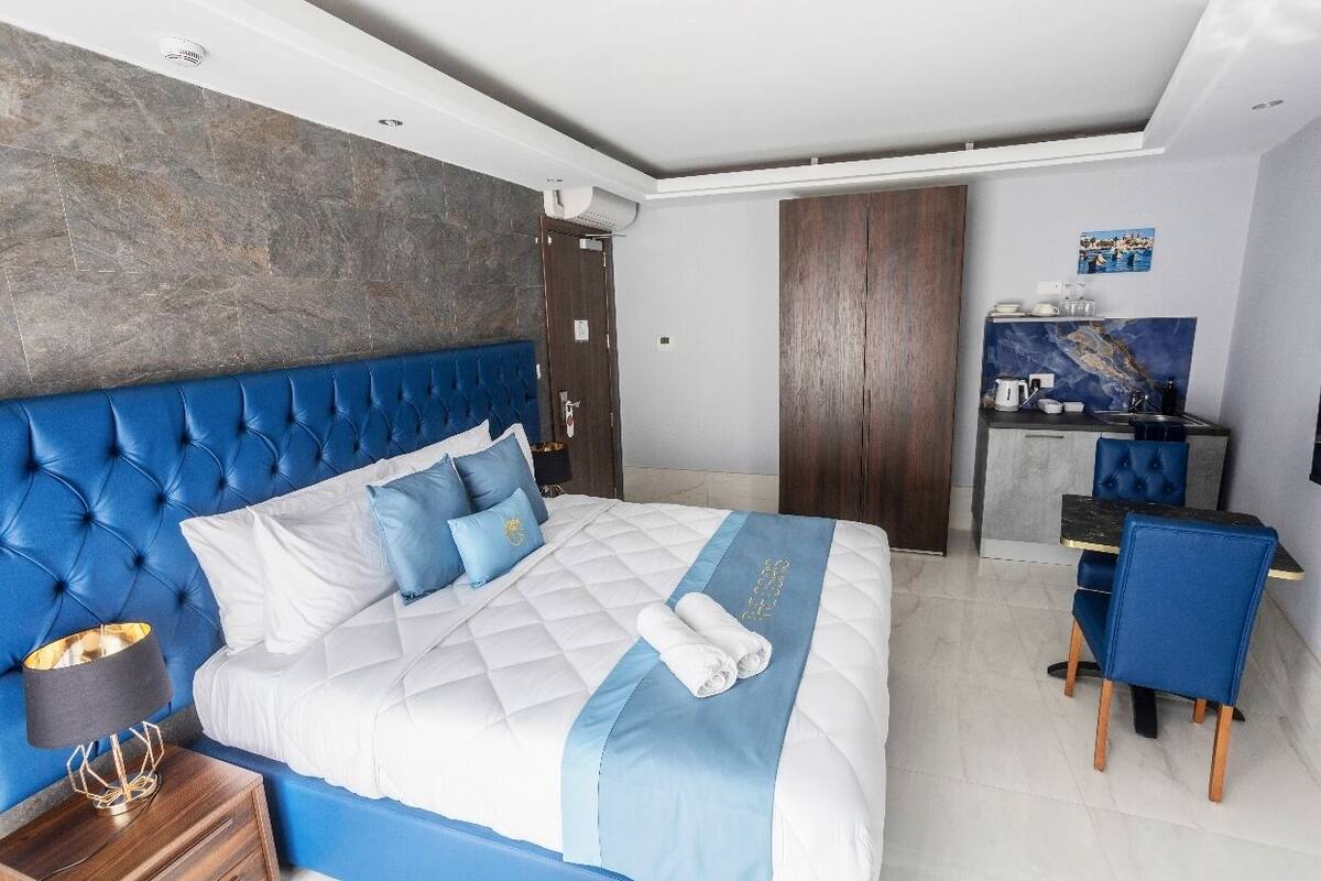 Une chambre d’hôtel moderne avec un grand lit, une tête de lit bleue, une table de chevet en bois et un petit bureau avec une chaise.