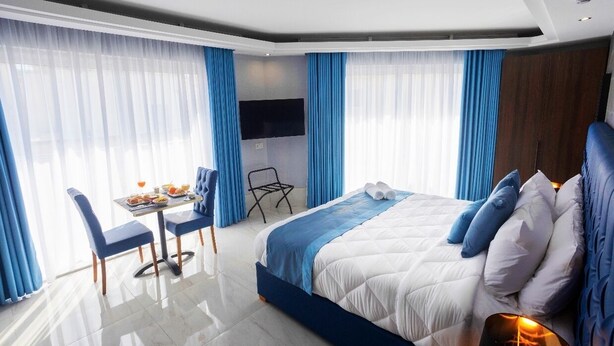 A modern hotel room with a large bed, a dining area with a table and chairs, and a TV mounted on the wall. - THE OSIRIS (Marsaxlokk)