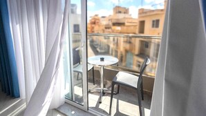 A balcony with a glass door, a small round table, and a chair, overlooking a cityscape. - THE OSIRIS (Marsaxlokk)