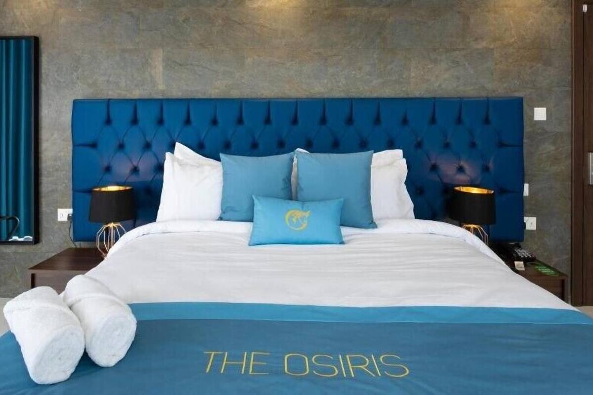 Une chambre d’hôtel avec un grand lit, une literie bleue et blanche, deux lampes de chevet et une tête de lit bleue.
