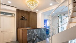 A reception desk with a wooden panel backdrop and a marble accent, a chandelier, and a spiral staircase. - THE OSIRIS (Marsaxlokk)