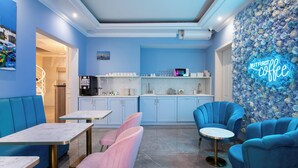 A modern interior with blue walls, a neon sign reading "BUTFIRST coffee", and seating areas with pink and blue chairs. - THE OSIRIS (Marsaxlokk)