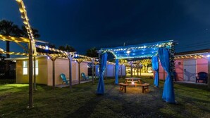 Un espace extérieur abrité, décoré de guirlandes lumineuses et de tentures bleues, avec un banc en bois et une petite table.